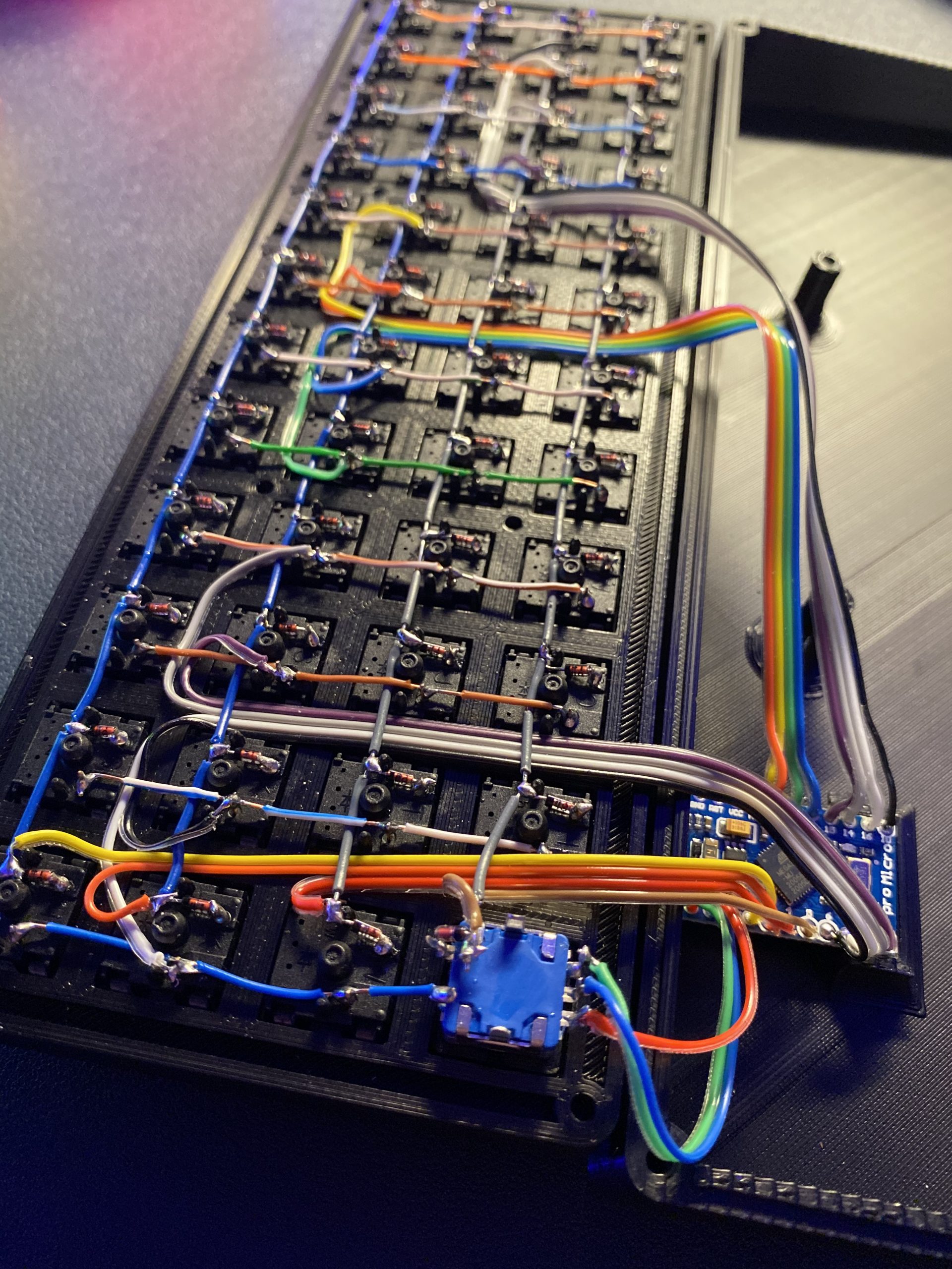 A picture from the back of the keyboard, showing the wired matrix and the link wires routed and connected to the microcontroller.