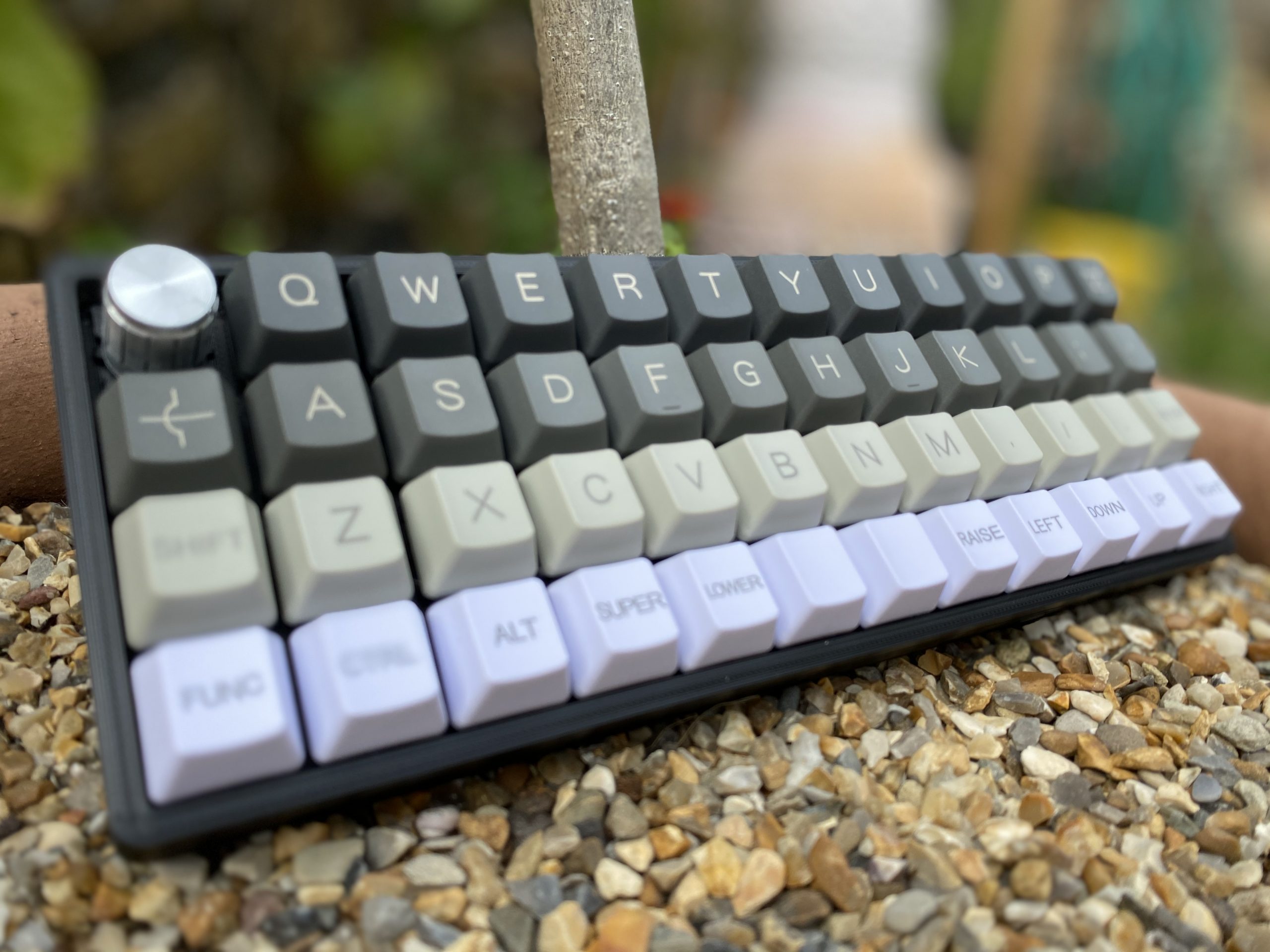 An image of the finished keyboard, laying on a plant pot full of gravel, that is sitting outside.