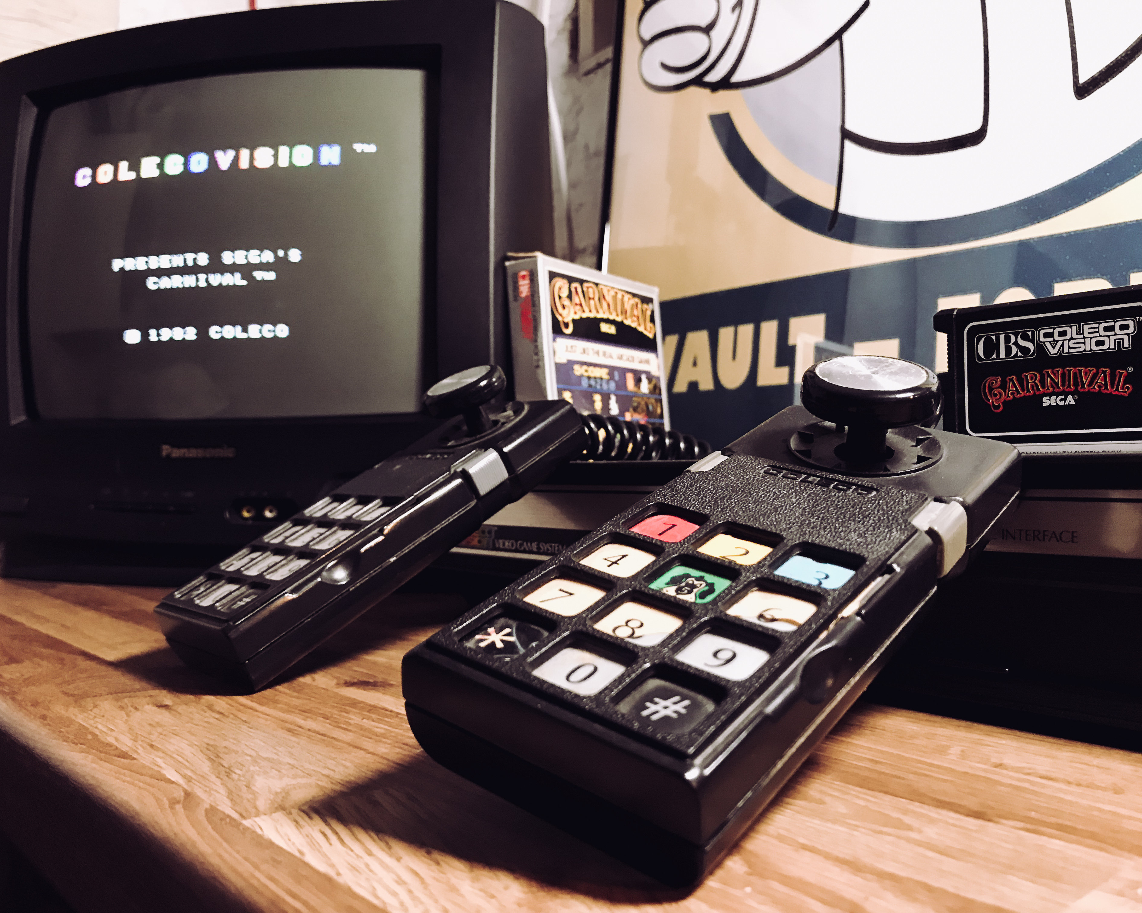 A picture of a ColecoVision console connected to a Panasonic CRT tv sat on a wooden desk in front of a Fallout game poster.