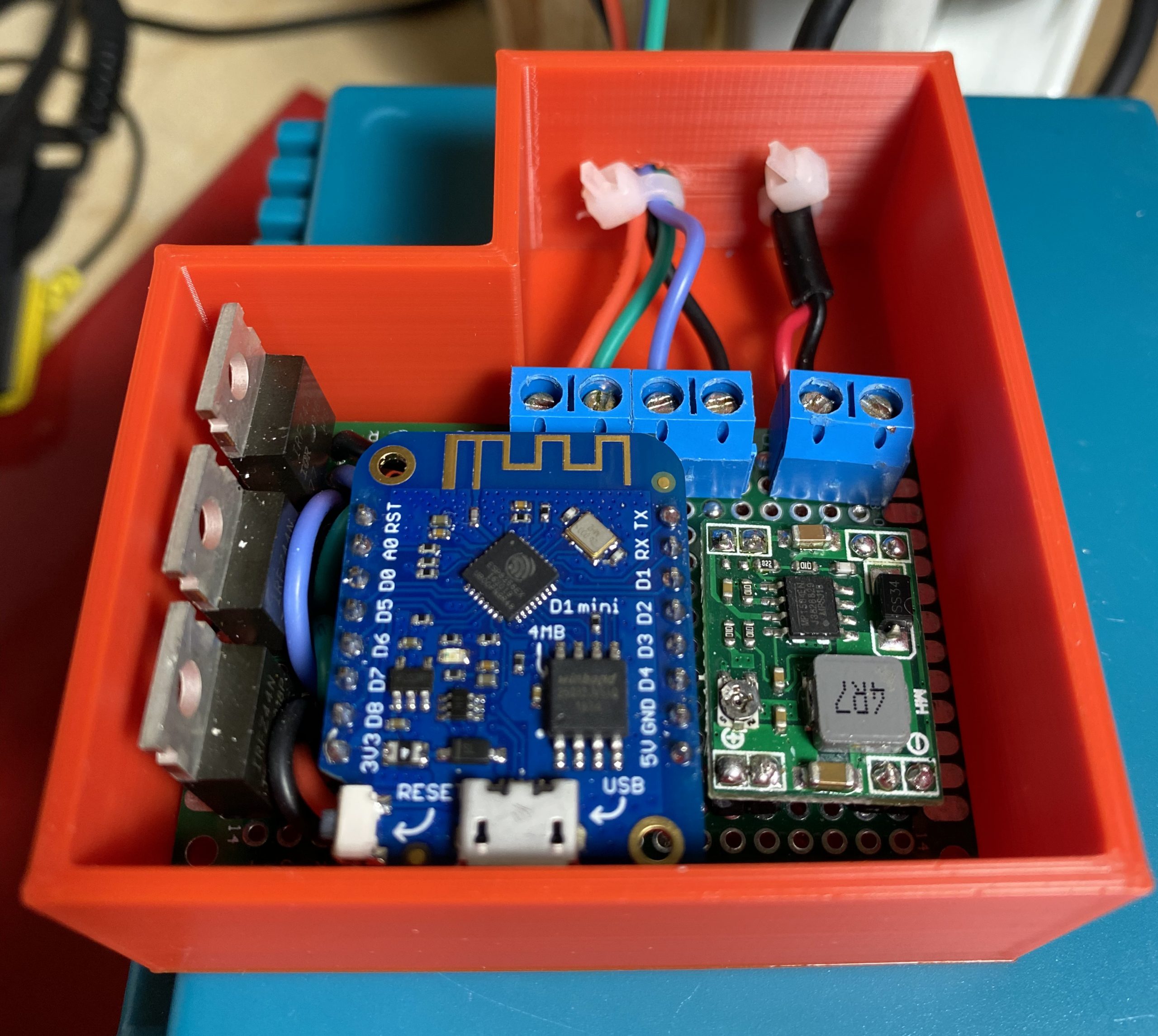 The completed circuit siting inside a red 3d printed case, all stat on a blue soldering mat