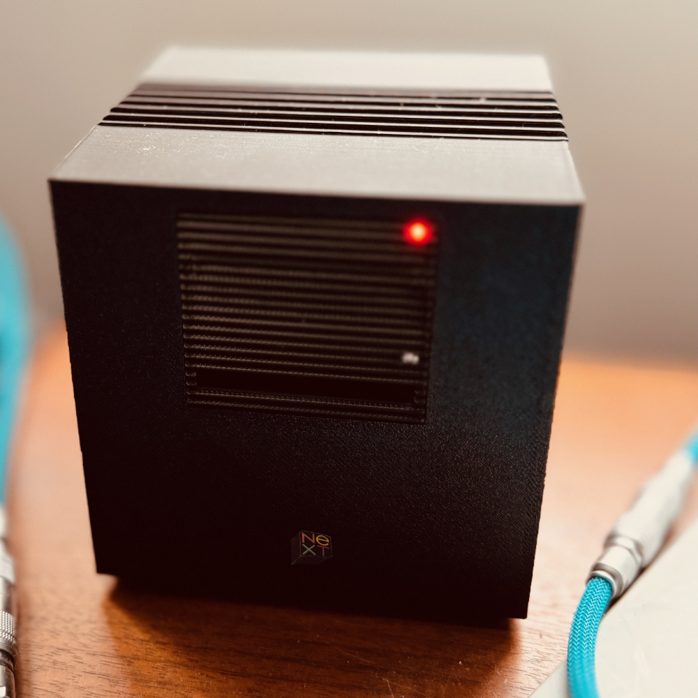 An image of a 3D printed NeXTcube replica, sitting on a desk between two monitors.