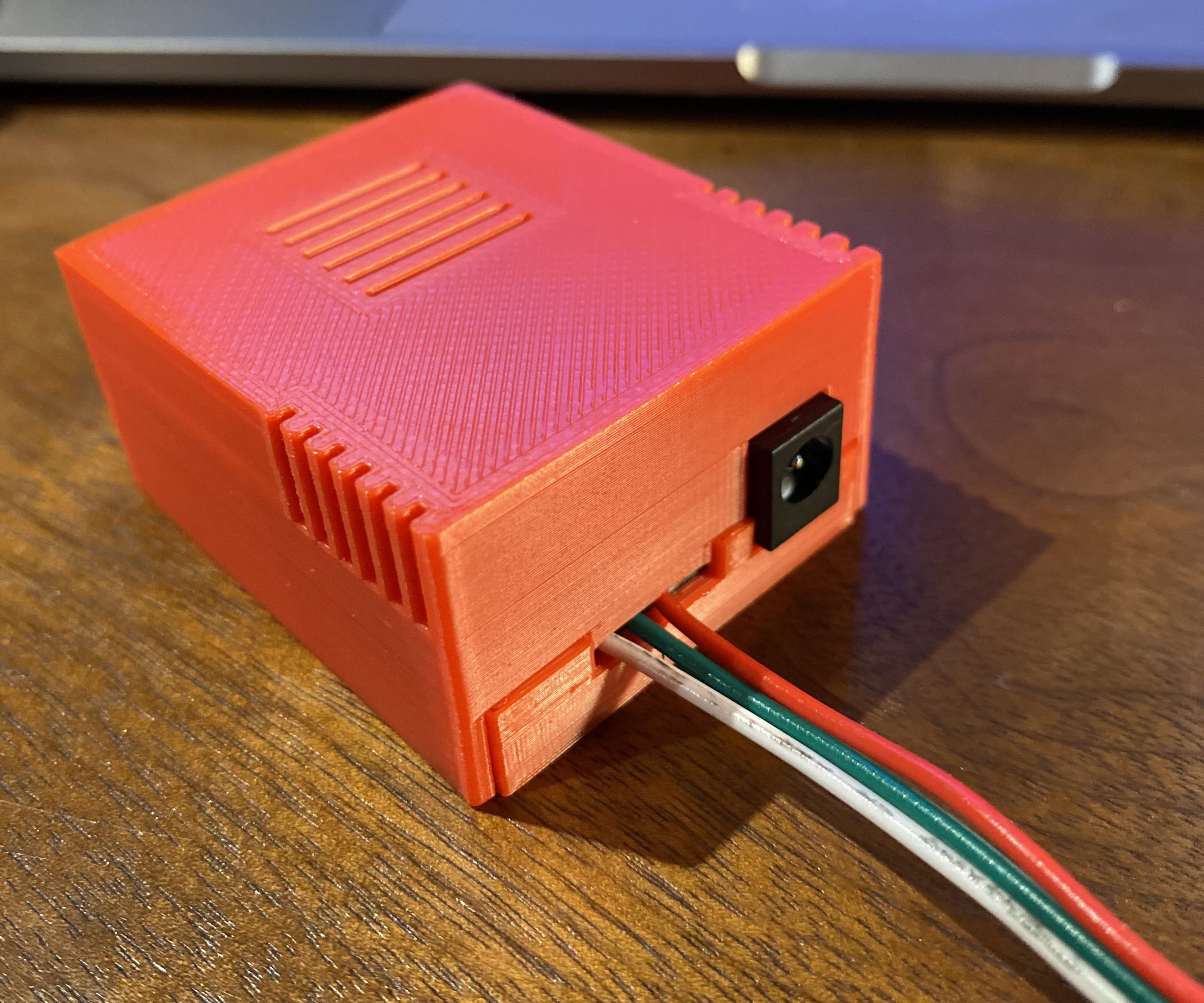 A picture of the neopixel circuit board, complete and sitting in a red 3d printed case on a wooden desk.