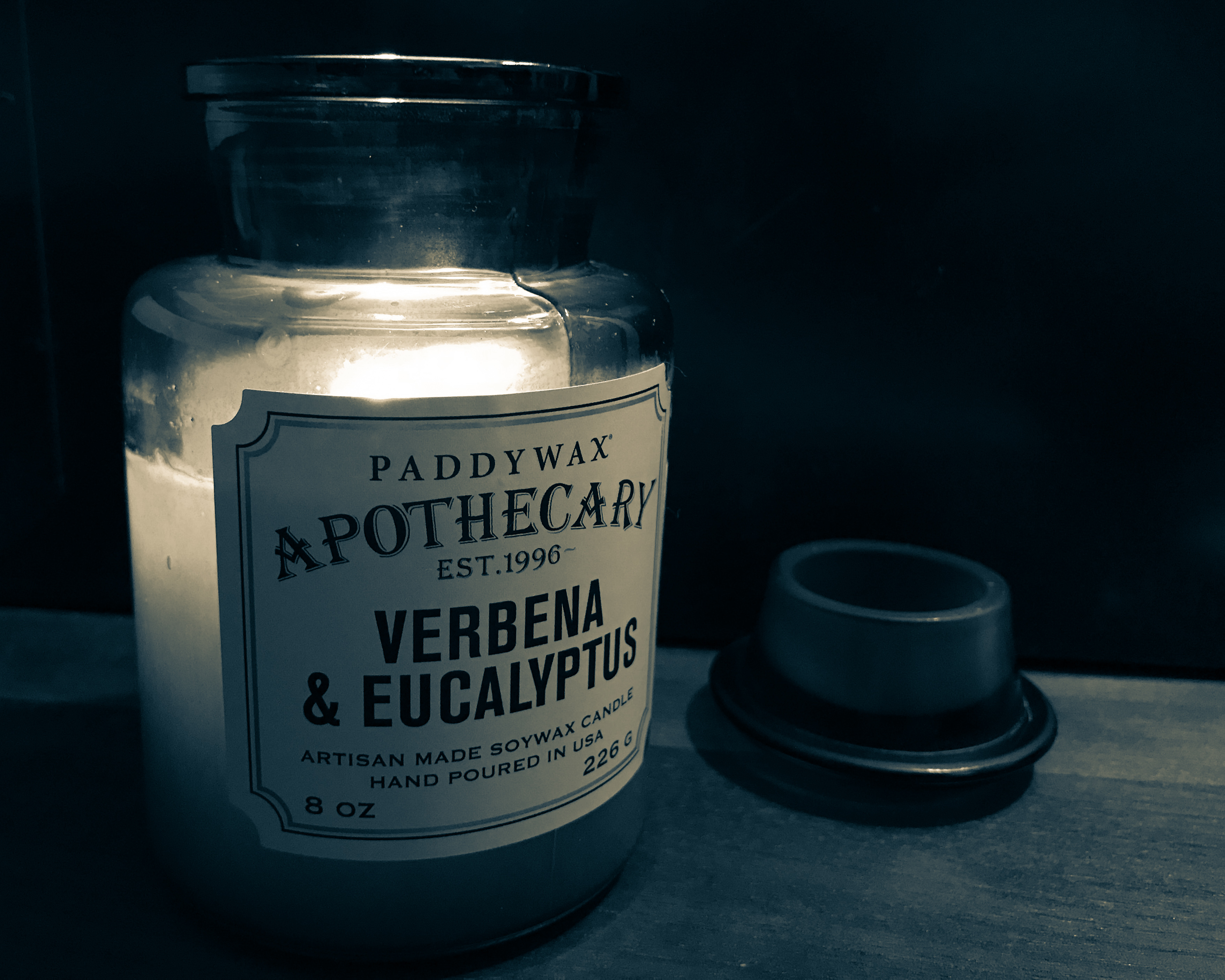 A sepia picture of a lit candle in an old apothecary jar sat on a desk.