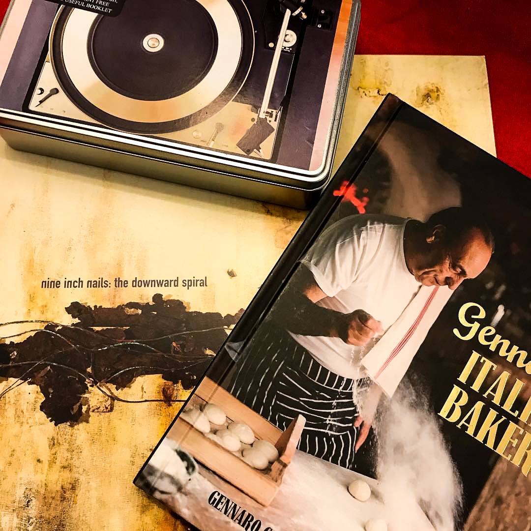 A picture of the vinyl of The Downward Spiral by Nine Inch Nails, sat on top of it is the book Gennaro&rsquo;s Italian Bakery and a record cleaning kit.  